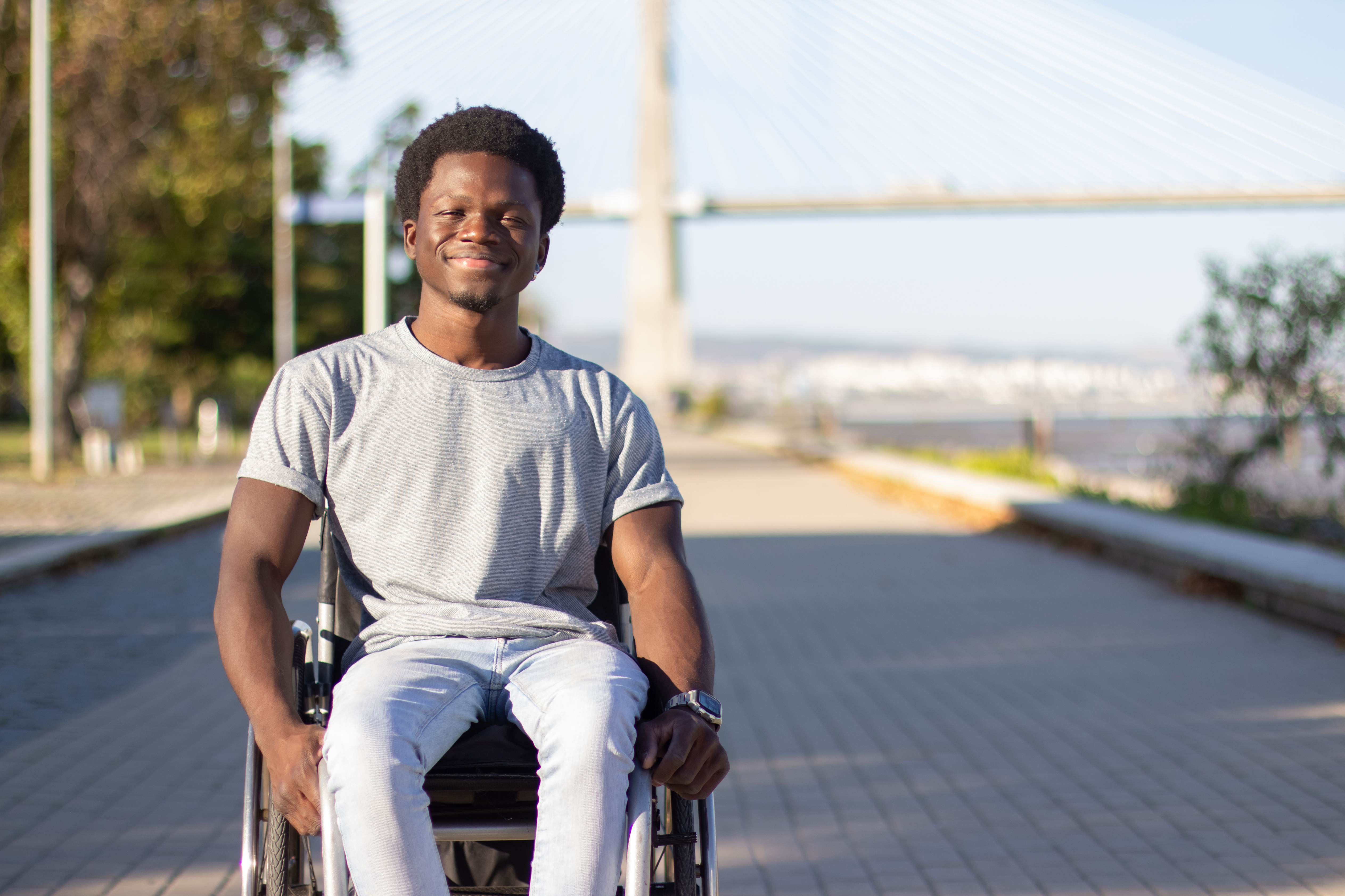 Homem negro jovem em cadeira de rodas aproveitando um dia quente de verão em um parque da cidade enquanto passeia pela estrada do parque
